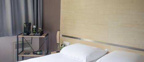 Una habitación de hotel con una cama, una mesita de noche con teléfono, una lámpara y un estante con artículos de aseo.