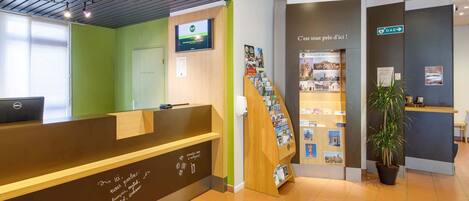 Una zona de recepción con mostrador de madera, pantalla digital, escalera y exhibición de folletos.