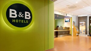 A reception area with a B&B Hotels sign, a reception desk, and a staircase leading to another floor.