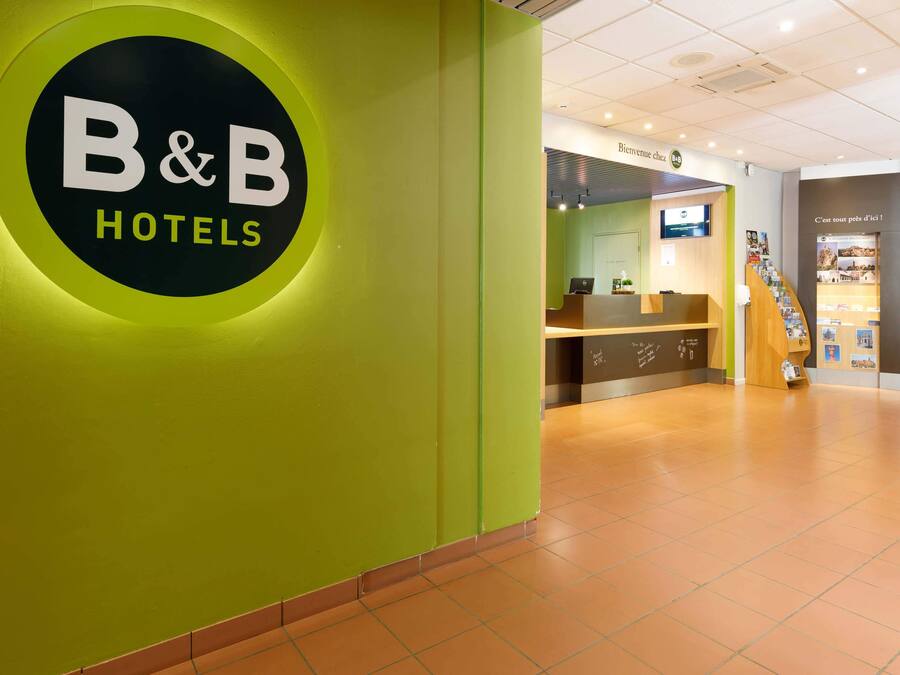 A reception area with a B&B Hotels sign, a reception desk, and a staircase leading to another floor.