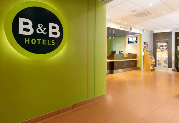 Una zona de recepción con un cartel de B&B Hotels, un mostrador de recepción y una escalera que lleva a otro piso.