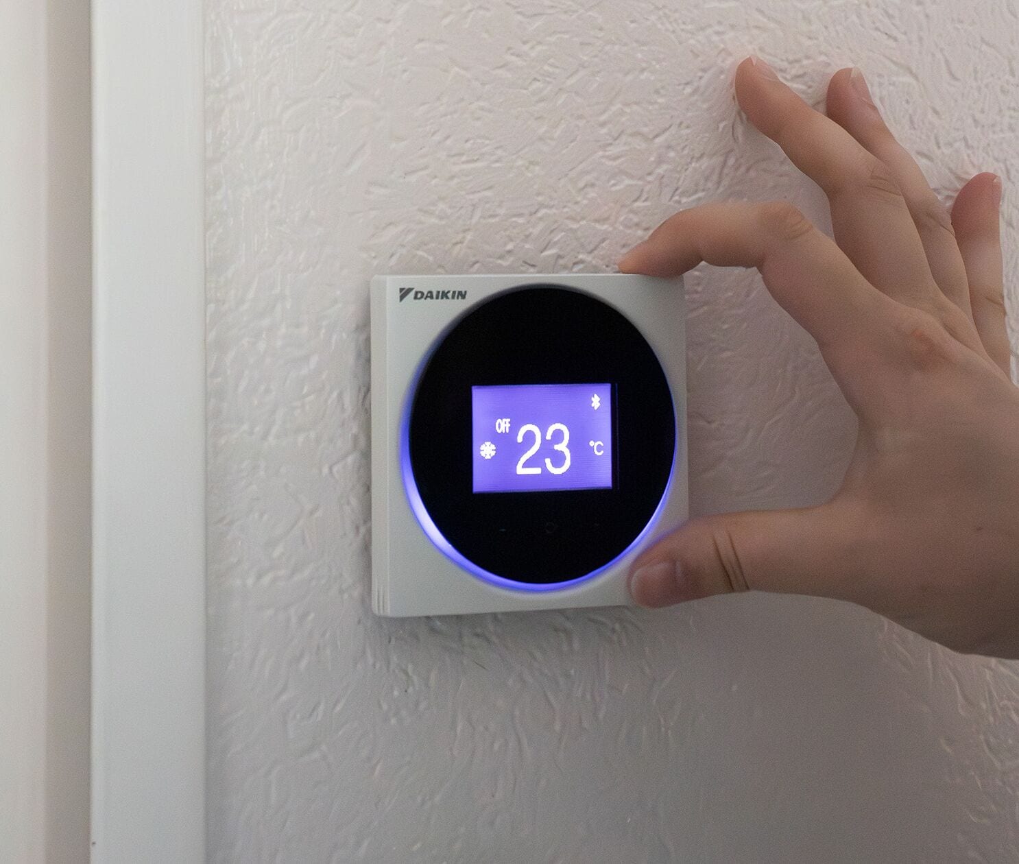 En hånd justerer termostaten på en væg med struktur.