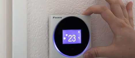 En hånd justerer termostaten på en væg med struktur.