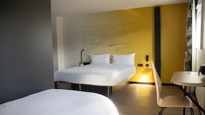 A hotel room with a bed, bedside table, chair, and a wall with a unique design.