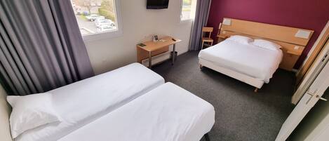 A hotel room with two beds, a desk, a TV, and a window with a view of parked cars.
