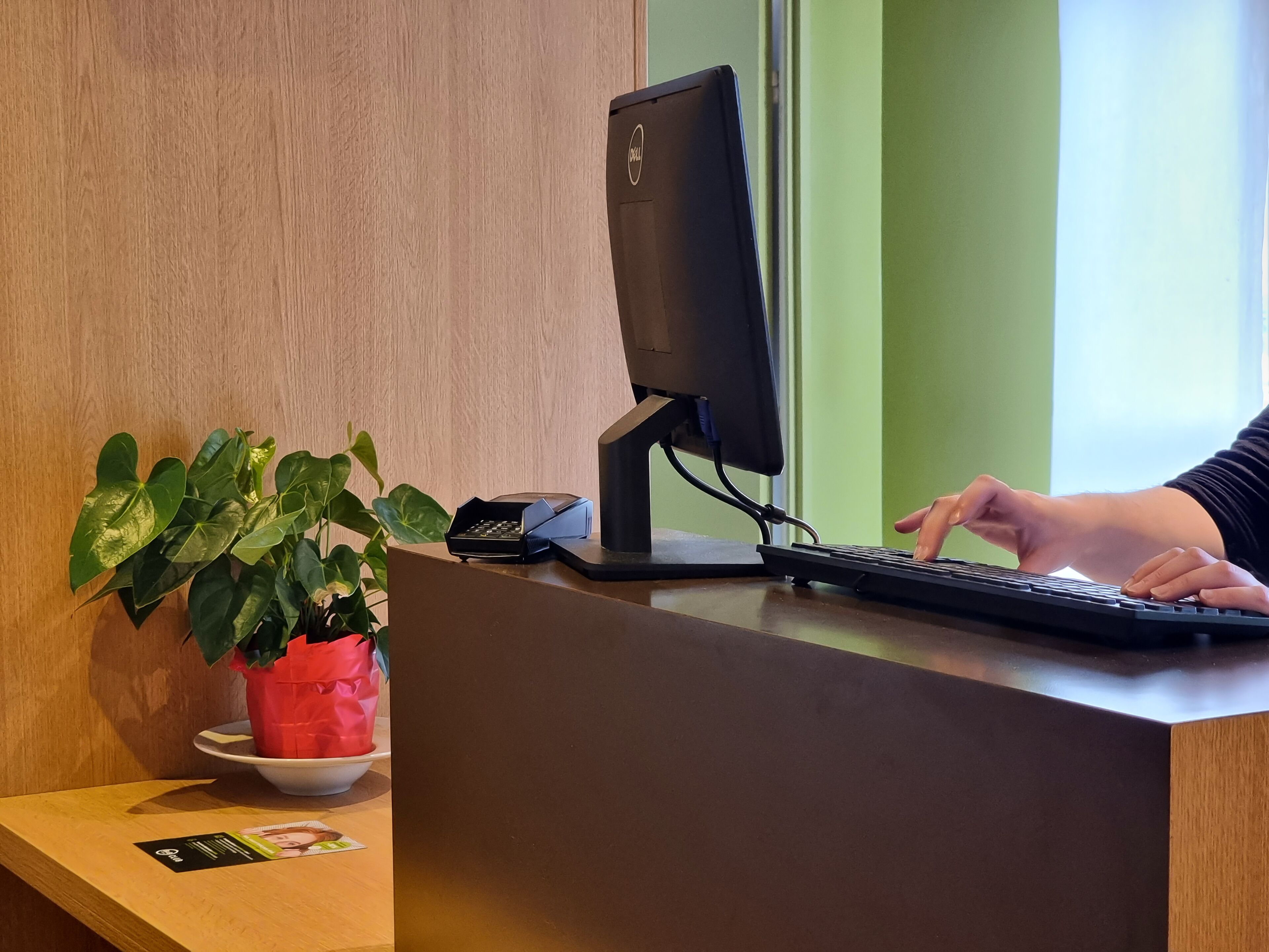 Un mostrador de recepción con un monitor de computadora, teclado y una planta en maceta.