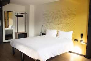 Una habitación de hotel moderna con una cama grande, una mesita de noche, un espejo y un teléfono instalado en la pared.