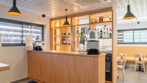 A bar area with a wooden counter, shelves with bottles, a coffee machine, and hanging lights.