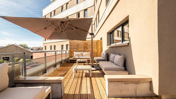 A rooftop terrace with a wooden deck, outdoor seating, and a large umbrella.