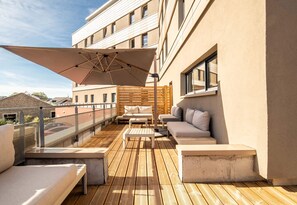 A rooftop terrace with a wooden deck, outdoor seating, and a large umbrella. - B&B HOTEL Limoges Gare (Limoges)