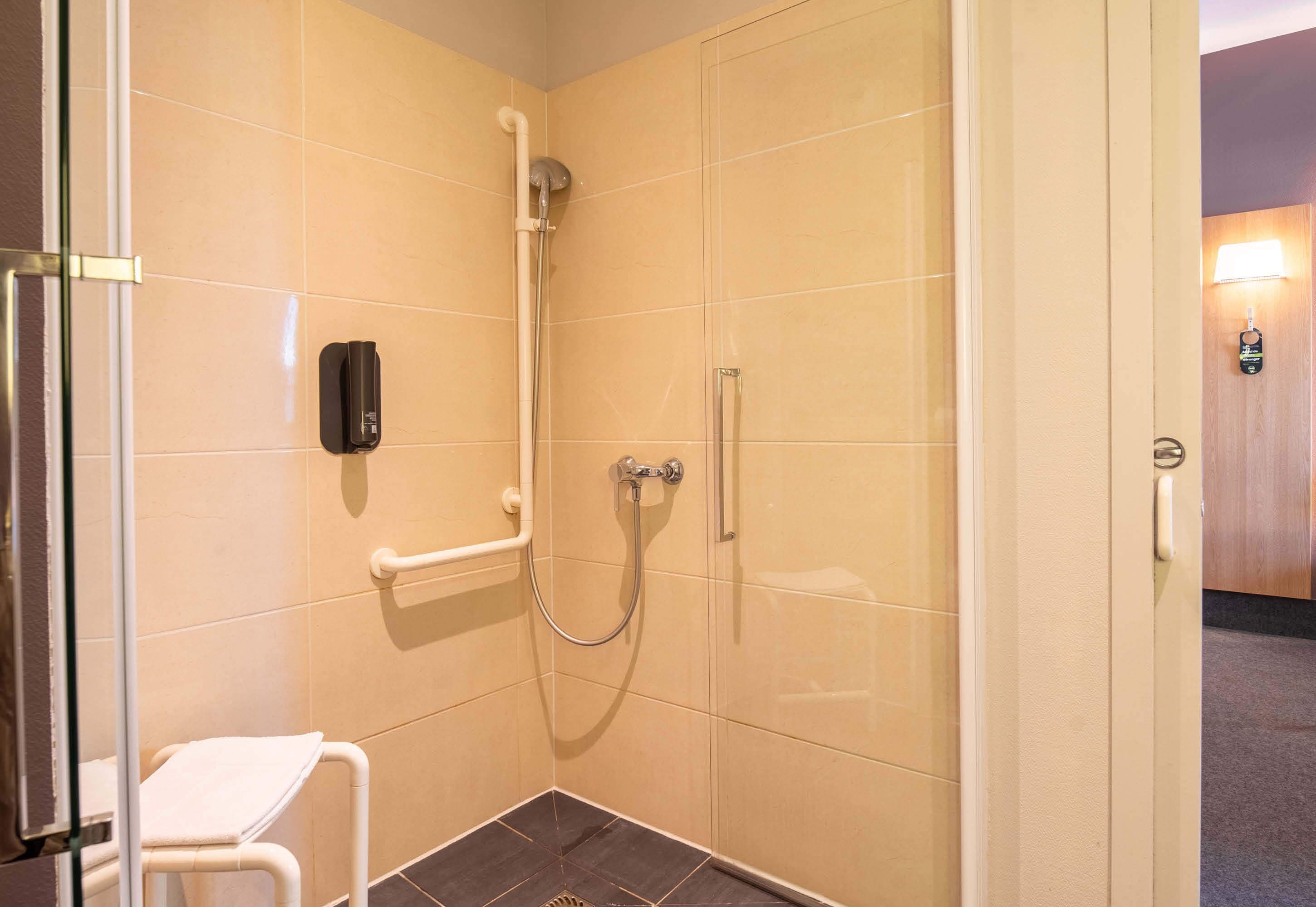 A small, enclosed shower area with a handheld showerhead, a handheld shower attachment, and a white towel on a stool.