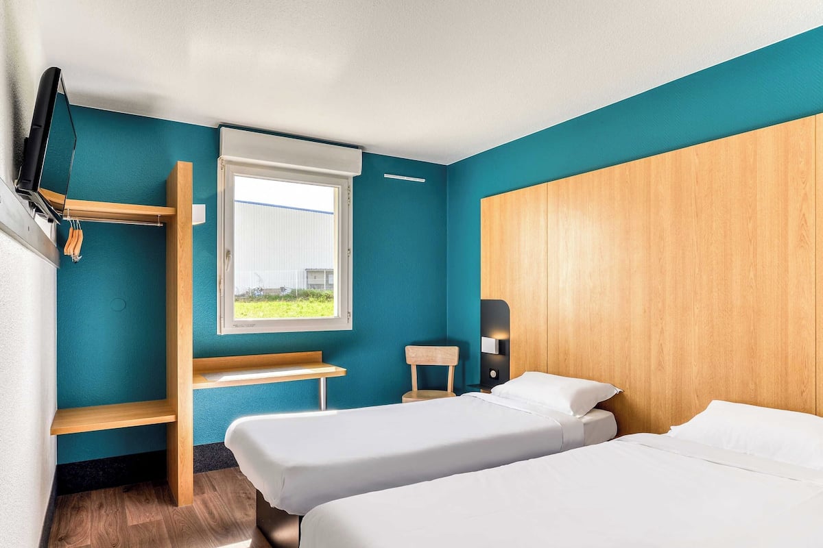 Une chambre d’hôtel avec deux lits, une télévision, une fenêtre et une tête de lit en bois.