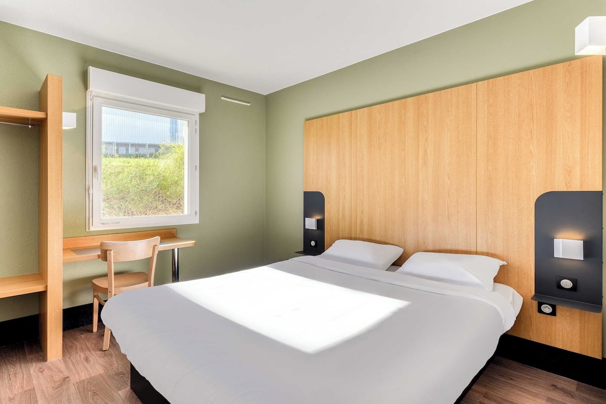 Une chambre d’hôtel moderne avec un grand lit, un bureau et une fenêtre donnant sur un paysage verdoyant.