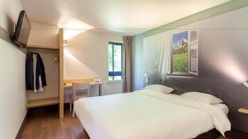 A hotel room with a bed, a desk, a chair, and a TV mounted on the wall.