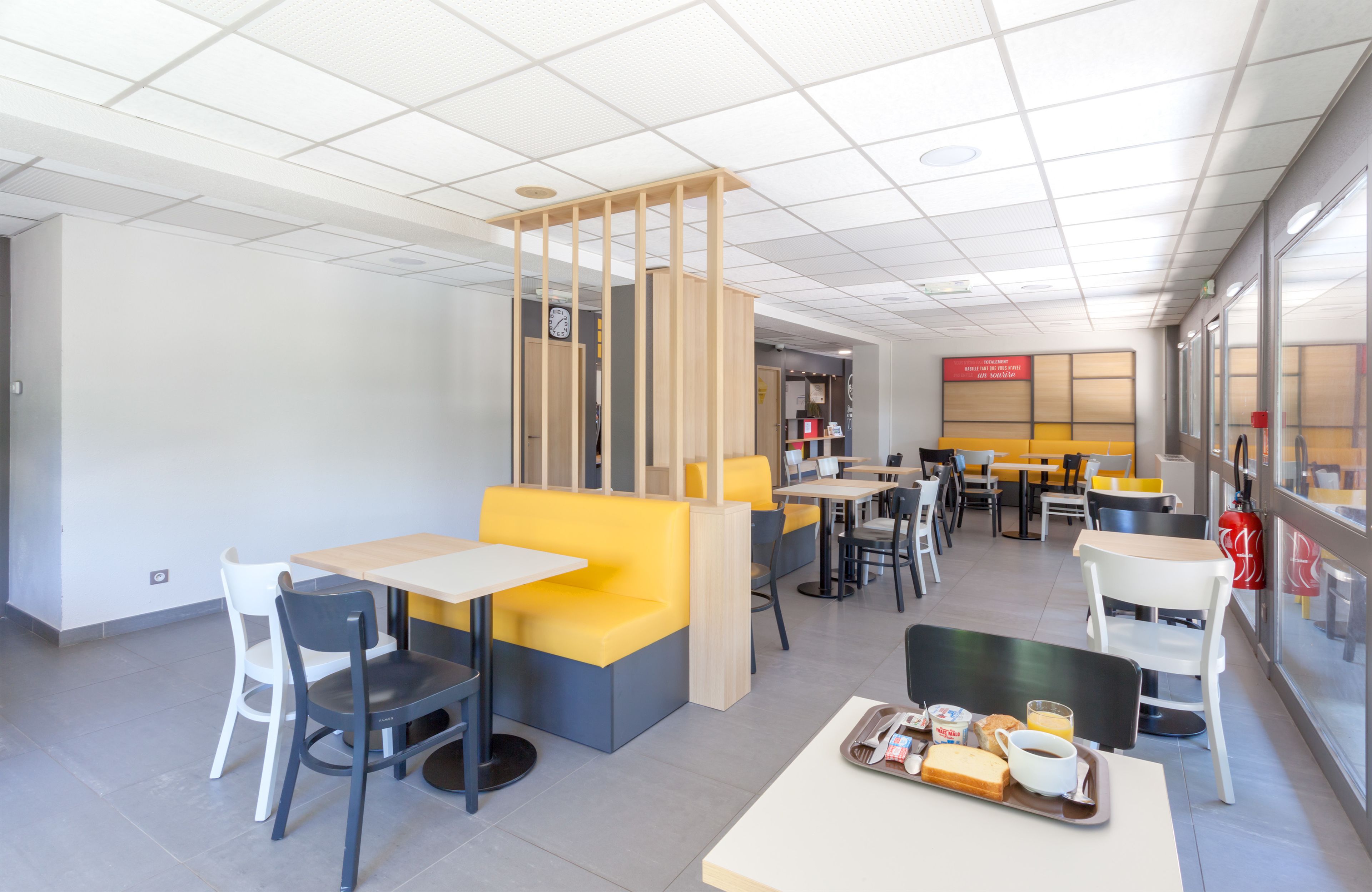 Un café moderne avec des sièges jaunes et gris, des tables blanches et un sol carrelé, propre et élégant.