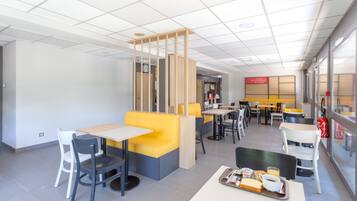 Un café moderne avec des sièges jaunes et gris, des tables blanches et un sol carrelé, propre et élégant.