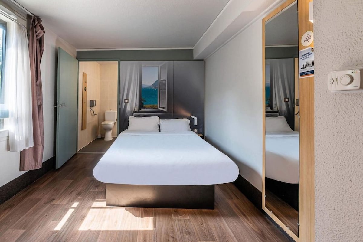 A modern hotel room with a large bed, a bathroom with a toilet and sink, and a view of the sea.