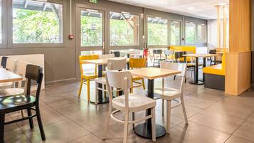 A modern dining area with tables and chairs, large windows with a view of greenery, and a fire extinguisher on the wall.