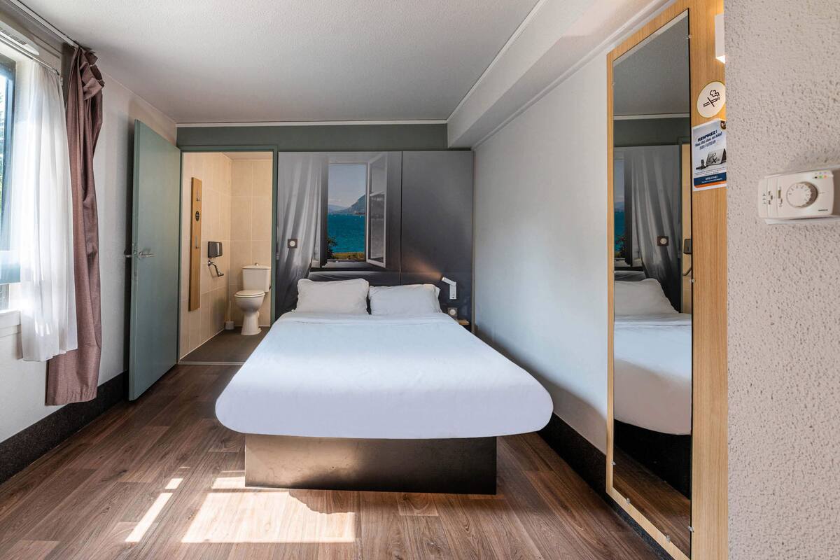 Une chambre d’hôtel moderne dotée d’un grand lit, d’une vue sur la mer, d’une salle de bain avec des toilettes et d’un miroir.
