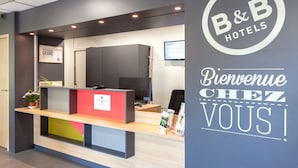 A reception desk with a B&B Hotels logo, a welcome sign, and a digital screen displaying room information. - B&B HOTEL Chambéry La Cassine (Chambery)