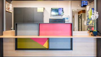 A reception desk with a flat-screen TV, a Samsung monitor, and a digital display.
