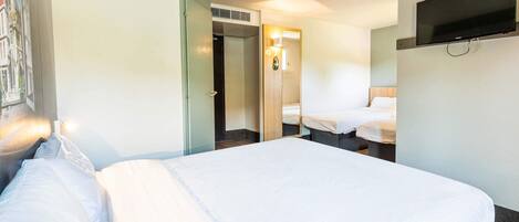 Habitación de hotel con una cama grande, un televisor montado en la pared y una puerta que da a un baño.