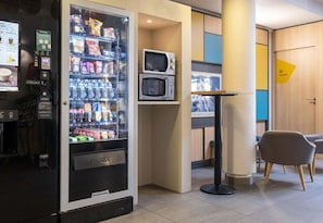 A vending machine with a 'PUSH' button, a microwave, and a seating area with a chair. - B&B HOTEL Annecy Argonay (Argonay)