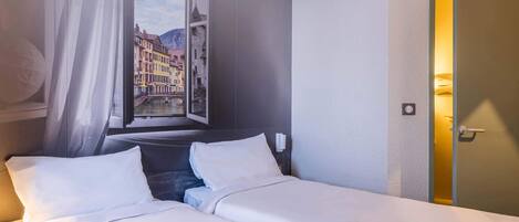 Una habitación de hotel con una cama, un ventanal con vistas a edificios y una puerta.