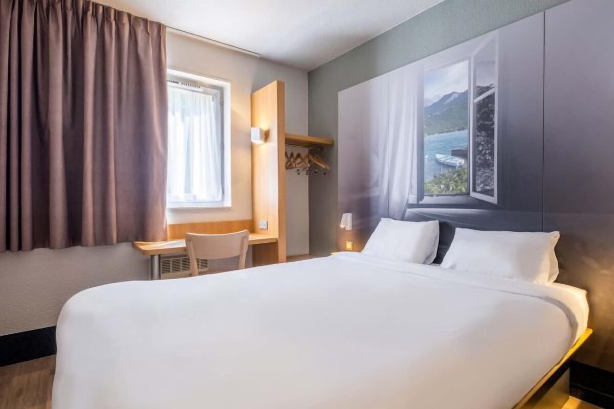 A hotel room with a large bed, a desk, a chair, a window with a view of the sea, and a wardrobe.