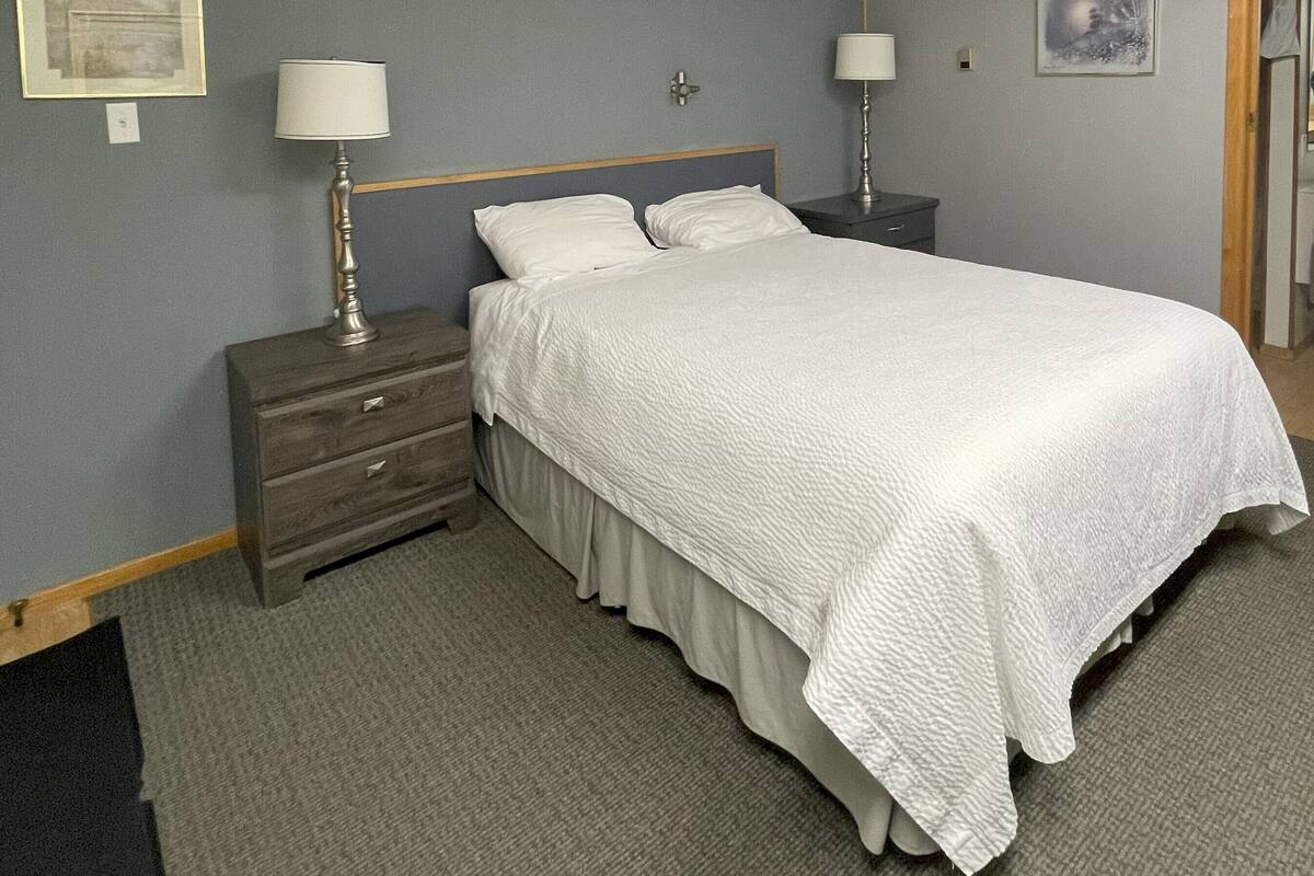 Una habitación de hotel ordenada con una cama, dos mesitas de noche y un aparador.