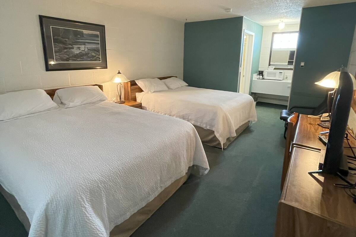 Habitación de hotel con dos camas, un escritorio con una computadora, una lámpara y un cuadro en la pared.