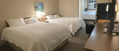A hotel room with two beds, a desk with a computer, a lamp, and a painting on the wall.