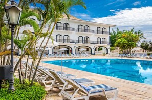 A pool area with lounge chairs and a white building with balconies.