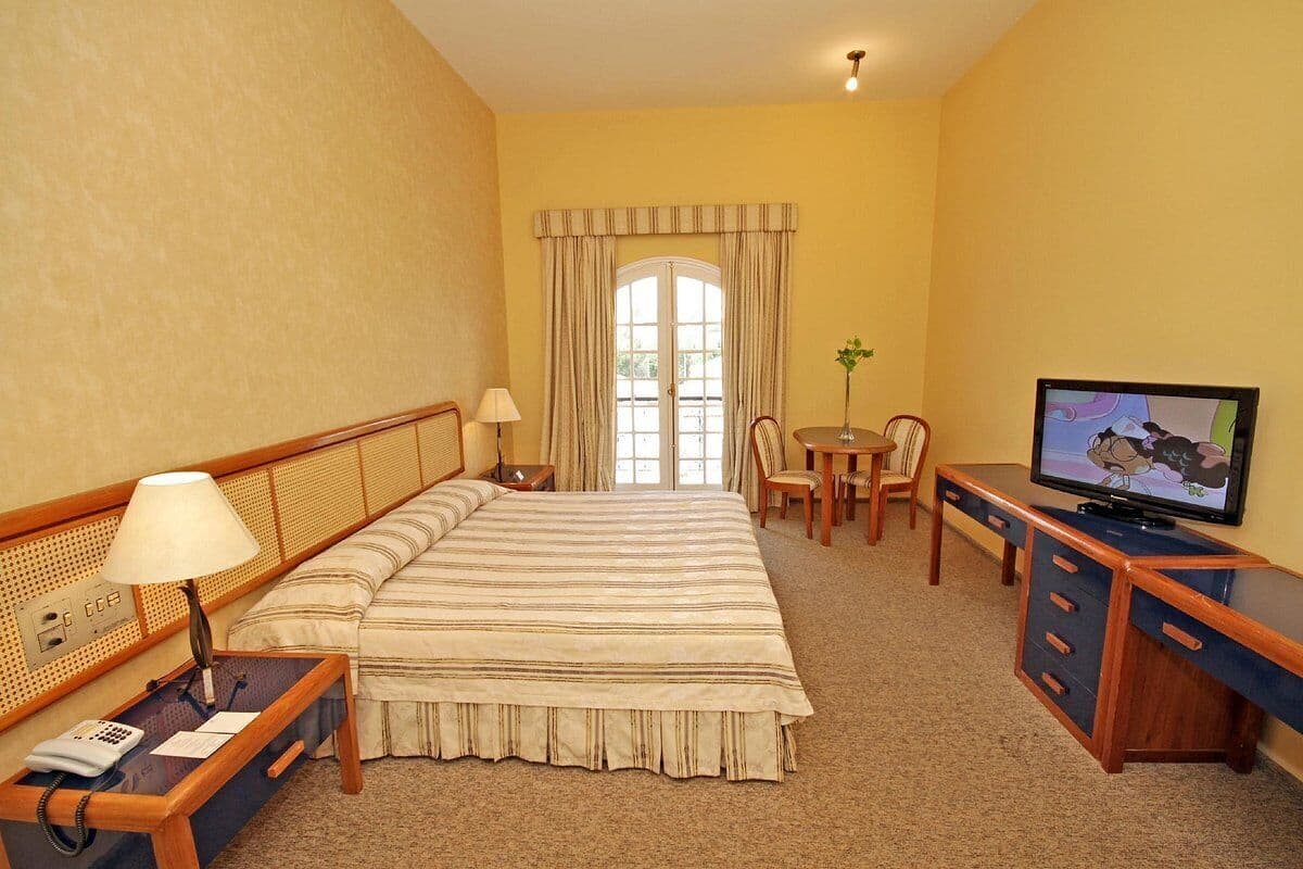 Habitación de hotel con cama, escritorio, televisor y una pequeña mesa con sillas.