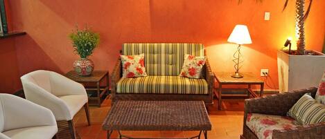 A cozy living room with a striped sofa, two white armchairs, a wicker coffee table, and a small side table with a lamp.