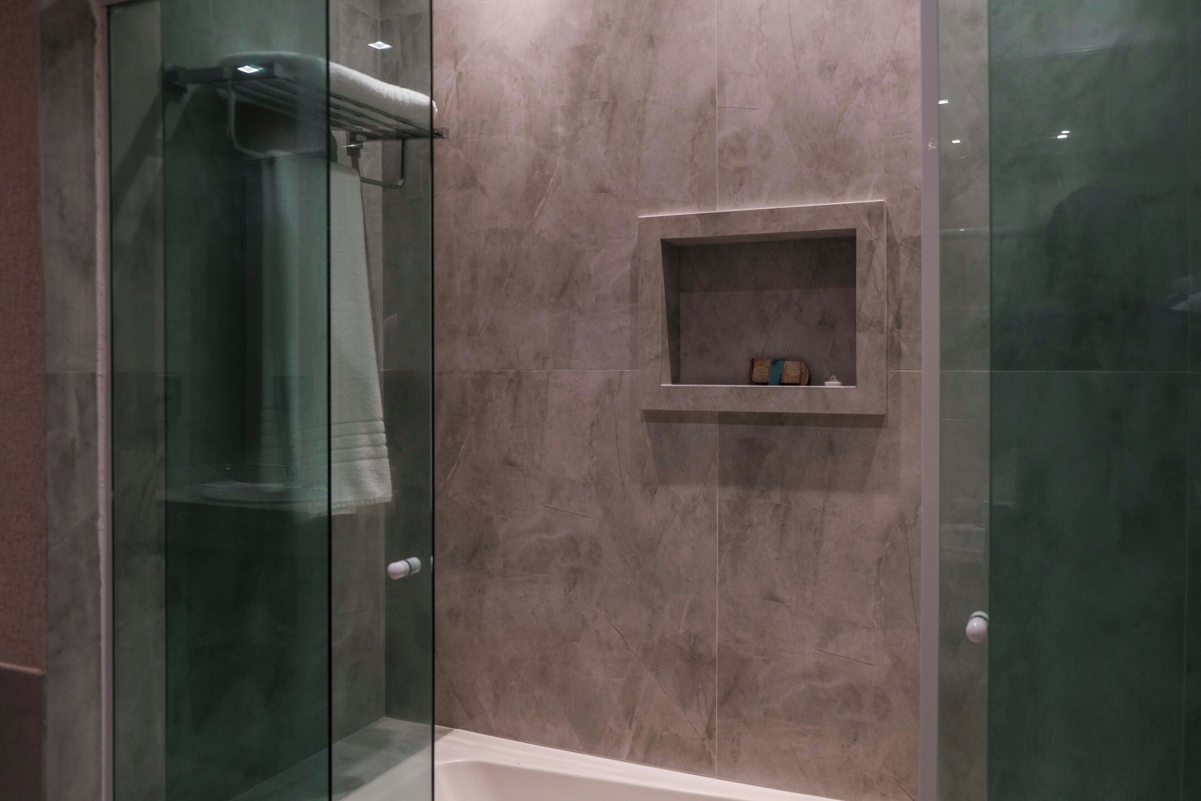 Un baño moderno con ducha envuelta en vidrio, paredes de mármol y un pequeño estante con artículos de aseo.