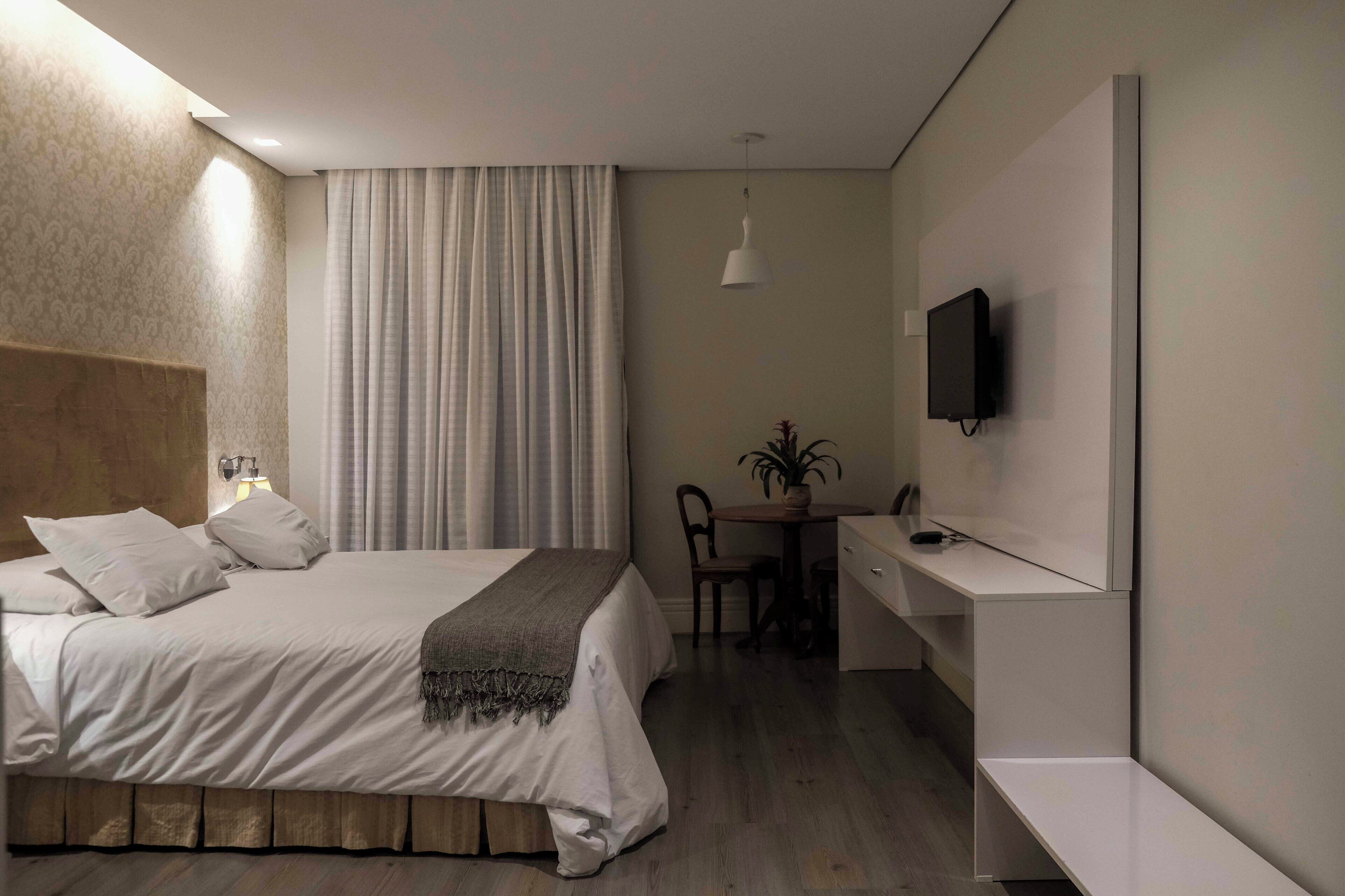 A modern hotel room with a large bed, a desk, a chair, a TV, and a plant.