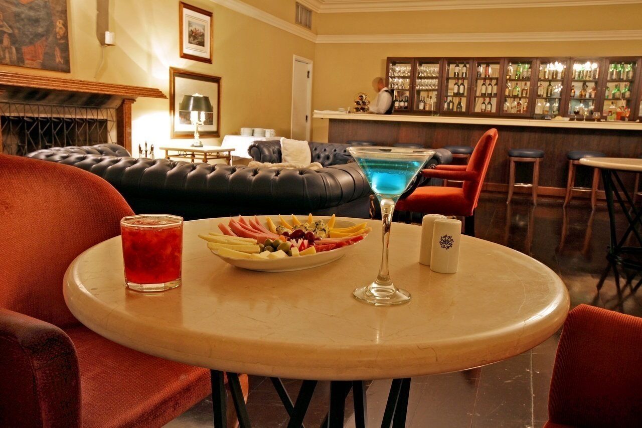 A bar area with a pool table, bar stools, and a variety of bottles and glasses on shelves.