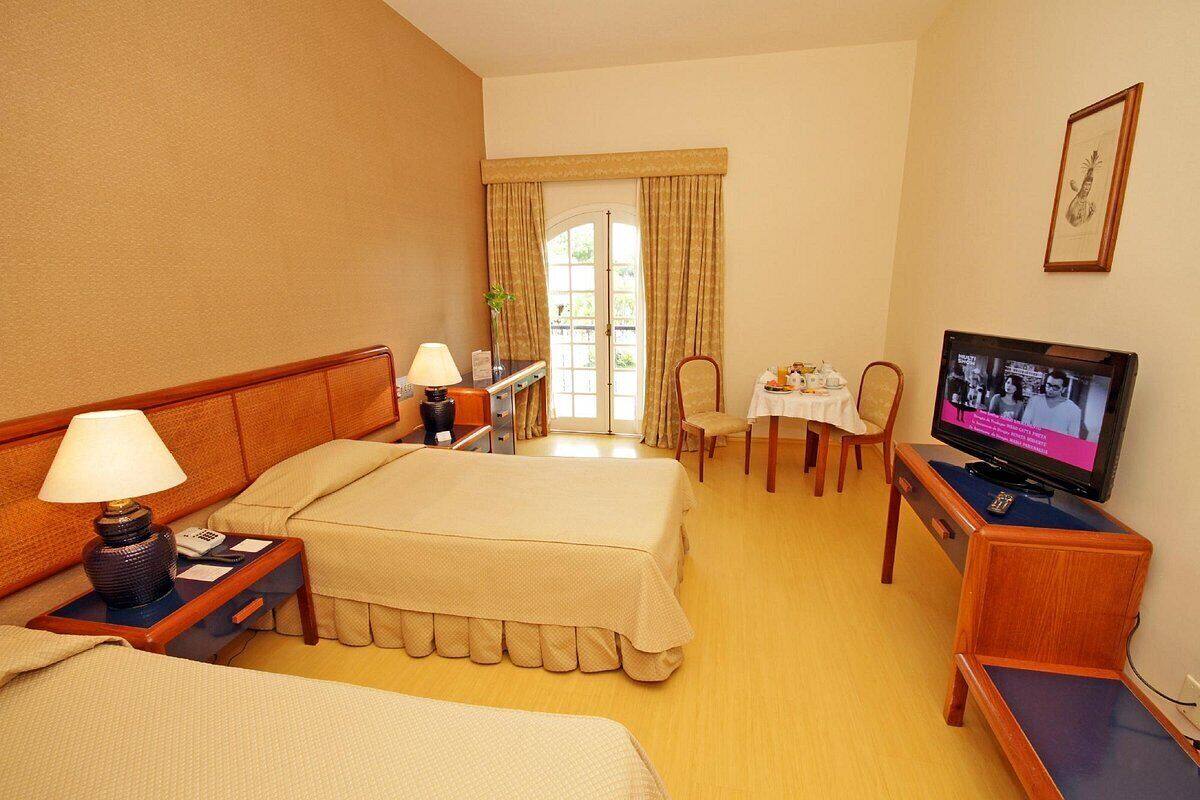 Habitación de hotel con dos camas, un escritorio con una silla, un televisor y una ventana con cortinas.