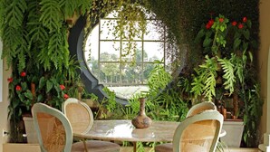 A dining area with a round table and four wicker chairs, surrounded by lush greenery and a large window. - San Raphael Country Hotel (Itu)