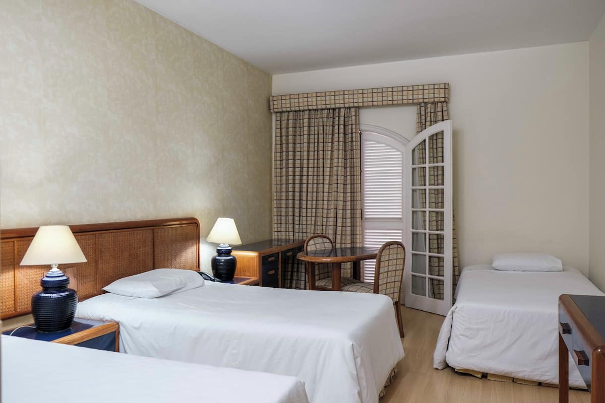 Habitación de hotel con dos camas, un escritorio, una silla y una ventana con cortinas.