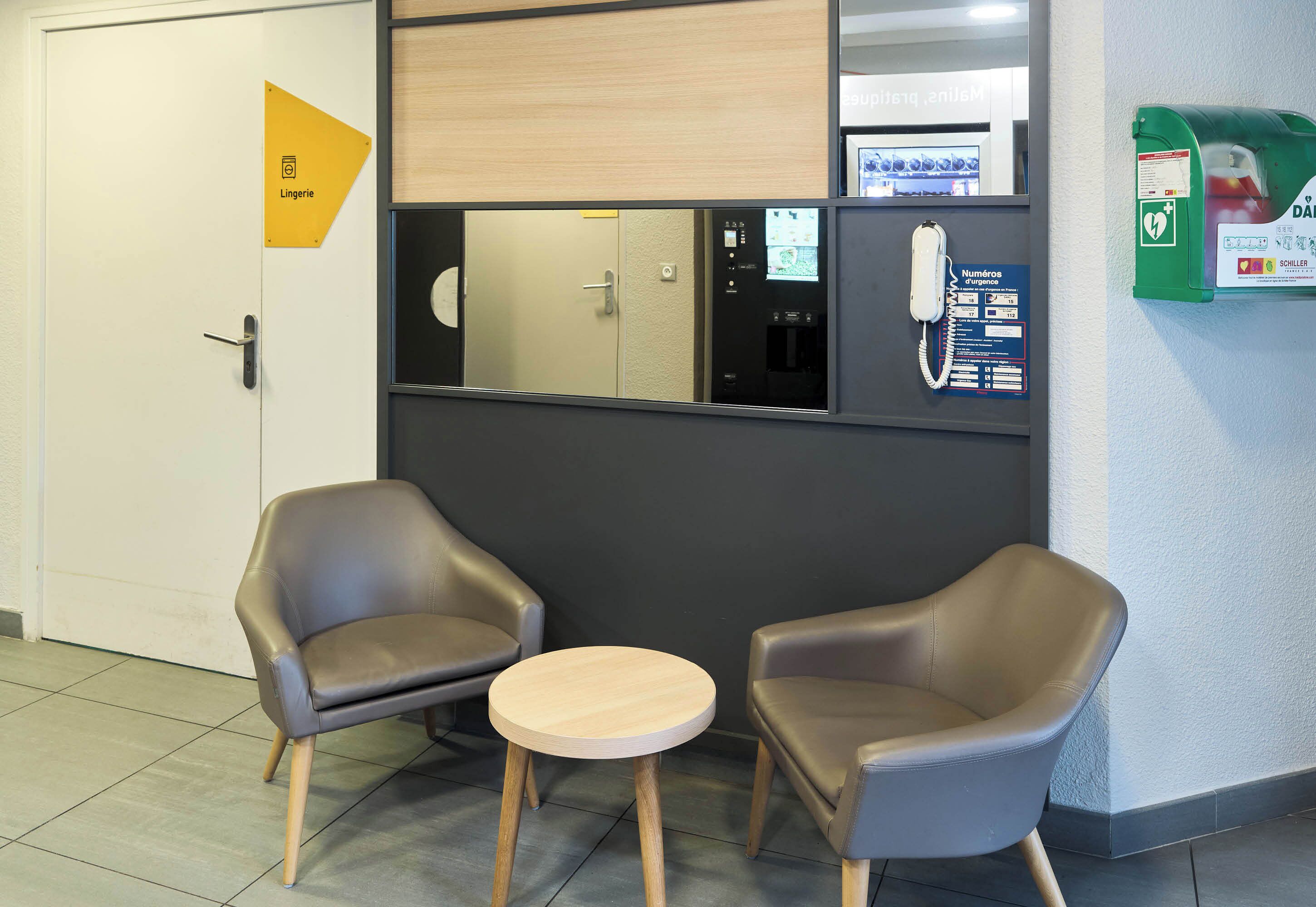 A reception area with two leather chairs, a small round table, a reception desk, a phone, and a green information kiosk.