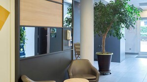 A modern waiting area with two leather chairs, a small round table, a large potted plant, and a wall-mounted telephone. - B&B HOTEL Saint-Michel-sur-Orge (Saint-Michel-sur-Orge)