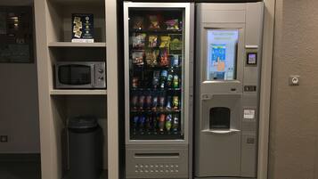 Un distributeur automatique proposant une variété de collations et de boissons, une poubelle et un four à micro-ondes situés au-dessus.