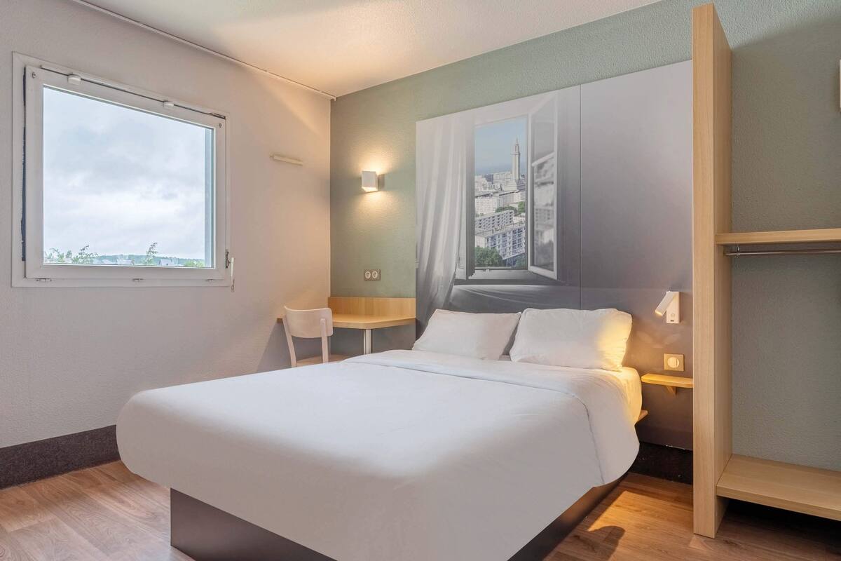 Een moderne hotelkamer met een groot bed, een raam met uitzicht op de stad, een klein tafeltje en een stoel.