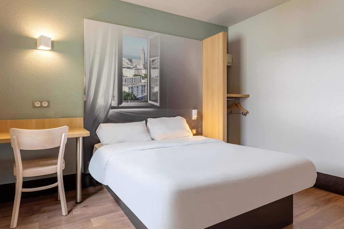 Een hotelkamer met een bed, een bureau en een stoel. Er is een raam met uitzicht op een stadsbeeld.