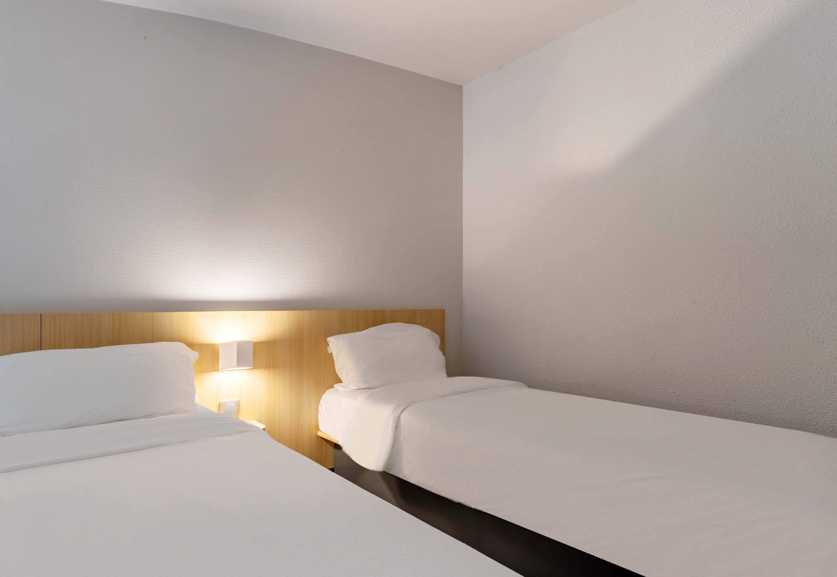 Una habitación de hotel con dos camas individuales, un cabecero de madera y una lámpara de noche.
