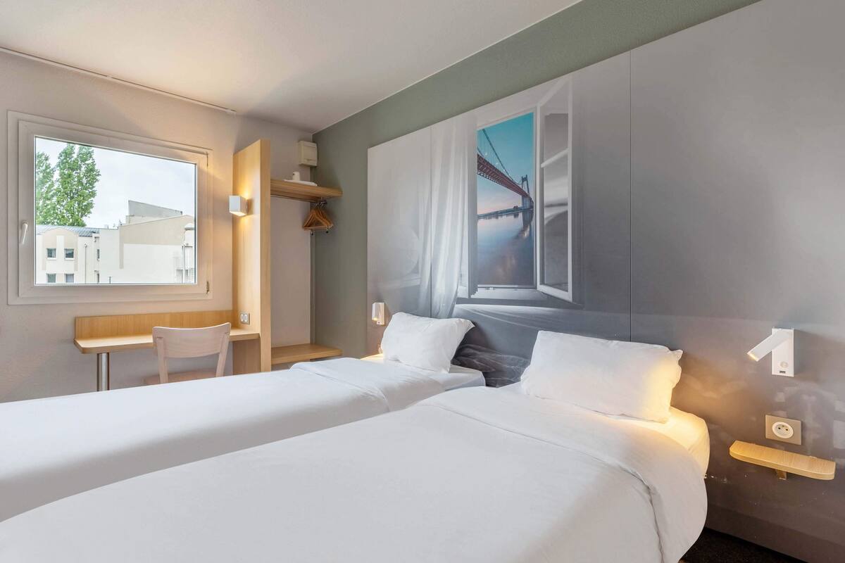 Een hotelkamer met twee bedden, een bureau en een groot raam met uitzicht op een brug.