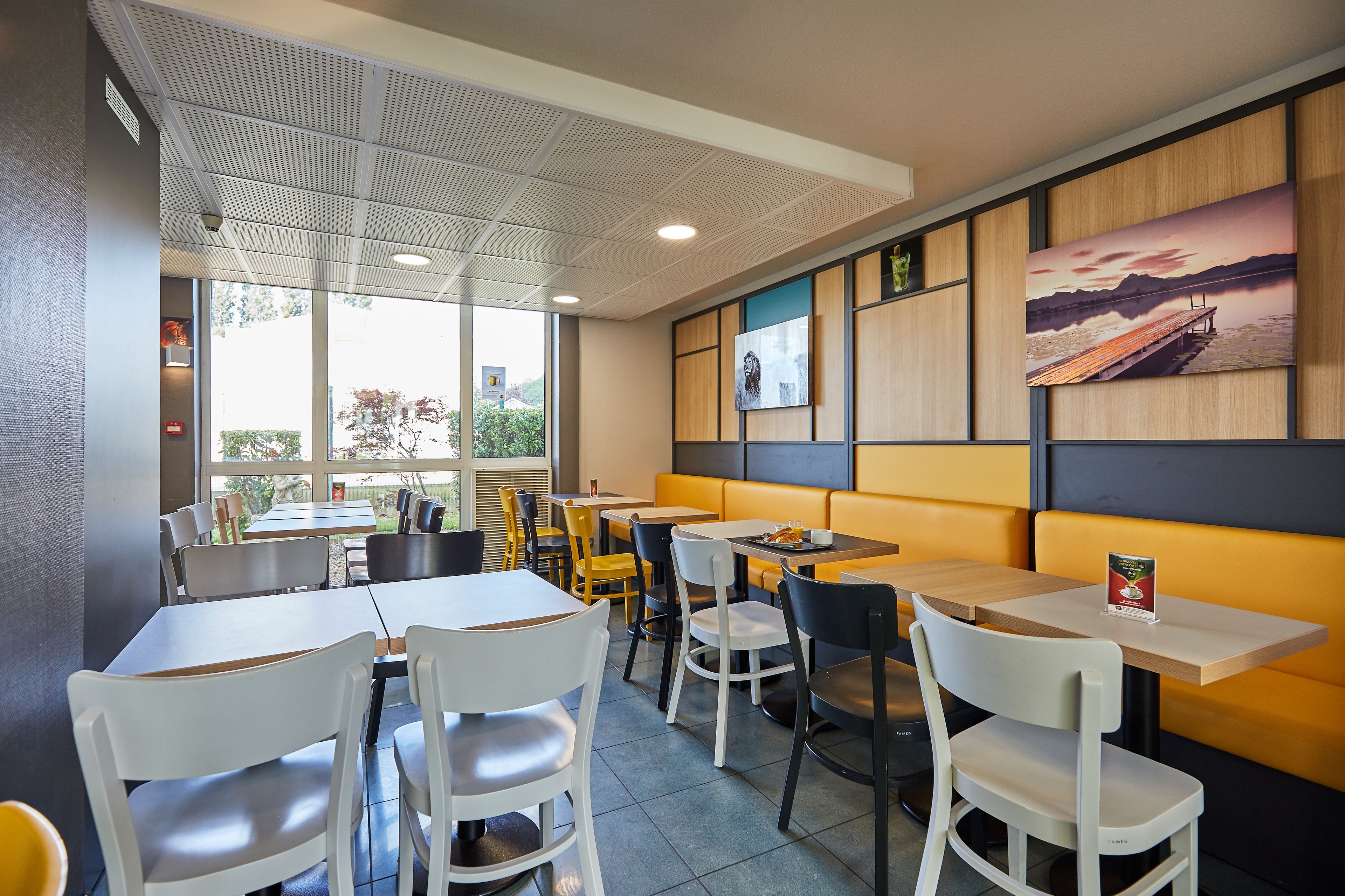 A restaurant interior with tables and chairs, a wooden accent wall, and a large window.