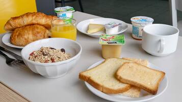 Una tavola imbandita per la colazione con croissant, cereali, pane tostato, yogurt e succo di frutta.